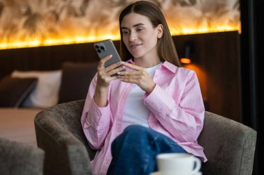 Huzurlu bir sabah. Elinde telefonla çay içen pembe elbiseli hoş bir genç bayan.