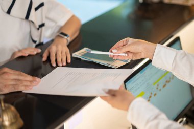 Giriş yap. Resepsiyon masasında dokümanları dağıtan ellerin resmini kapat.