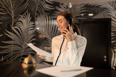 Resepsiyon. Müşteri için konaklama ayarlarken resepsiyonist telefonda konuşuyor.