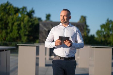 Açık havada düşünürken elinde tablet olan beyaz gömlekli yakışıklı bir adam.