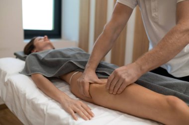 Anti-selülit bacak masajı. Masör kanepede uzanan bir kadına bacak masajı yapıyor.