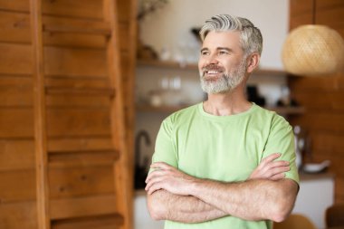 Orta yaşlı, gülümseyen, kollarını kavuşturmuş bir adam..
