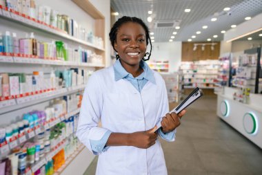 Eczacı iş başında. Eczanede gülümseyen esmer bir kadın eczacı.