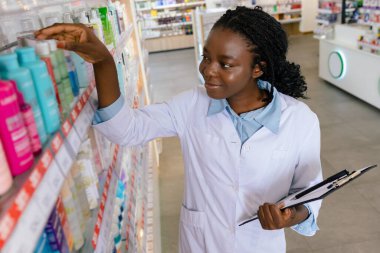 Eczacı iş başında. Genç gülümseyen eczacı eczanede envanter yapıyor.