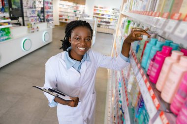 Eczacı iş başında. Genç gülümseyen eczacı eczanede envanter yapıyor.