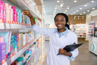 Eczacı iş başında. Genç gülümseyen eczacı eczanede envanter yapıyor.