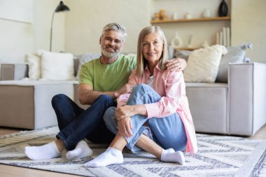 Oturma odasında oturmuş birlikte gülümseyen mutlu yaşlı çift.