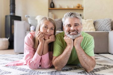 Yaşlı karı koca desenli halıya uzanıp kameraya mutlu bir şekilde bakıyorlar.