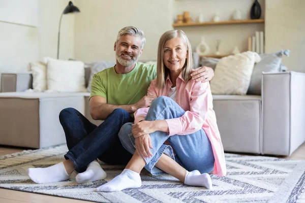 Oturma odasında oturmuş birlikte gülümseyen mutlu yaşlı çift.