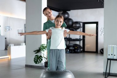 Kadın terapist ve çocuk ayakta durup kol egzersizi yapıyorlar.