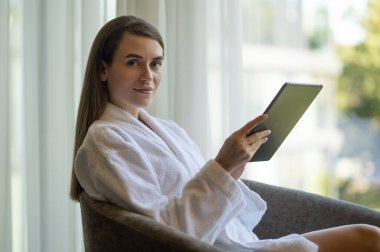 İletişim. Güzel beyaz bir kadın elinde tabletle koltukta oturuyor.