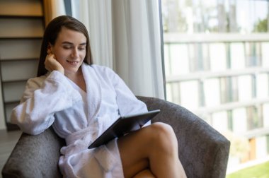 İletişim. Güzel beyaz bir kadın elinde tabletle koltukta oturuyor.