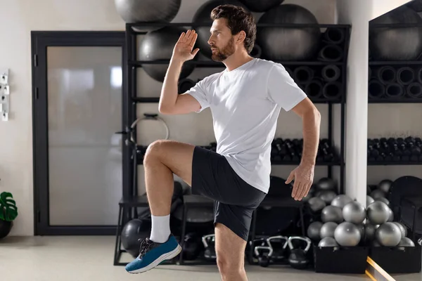 Spor salonunda. Sakallı genç adam spor salonunda egzersiz yapıyor ve odaklanmış görünüyor.