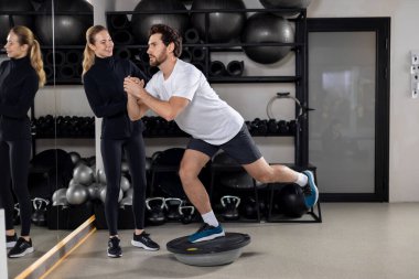 Denge tahtası egzersizi. Denge tahtasındaki adam, kadın koç ona yardım ediyor.