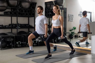 Hamleler. Genç adam ve kadın halterlerle egzersiz yapıyor ve ileri doğru hamle yapıyorlar.