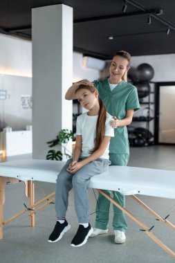 Terapi hareketi. Küçük bir kızın yanında duran kadın terapist boyun egzersizi yapıyor.