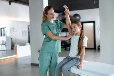 Kol esnekliği. Kadın terapist, küçük kızın koltuğa oturmasına yardım ediyor.