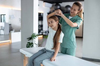Elle tedavi. Küçük kız boyun tedavisi uygulayan kadın terapist arkada oturuyor.