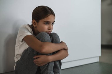 Çocuk depresyonu. Beyaz duvara yaslanmış, derin üzüntü ve çaresizlik hisseden genç bir kızın yakın plan portresi.