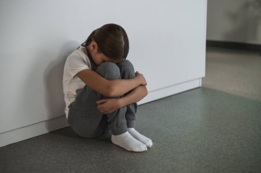 Okul zorbalığı. Sıkıntılı çocuk, köşede dizlerine sıkıca sarılıyor mağduriyetten reddedilme korkusu duyuyor.