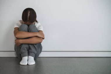 Akıl sağlığı. Yalnız bir kız yerde, kolları çapraz beyaz duvara yaslanmış, sessiz acı ve kaygı gösteriyor.