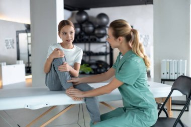 Rehabilitasyon sırasında genç bir kıza diz egzersizi yaptıran fizyoterapist.