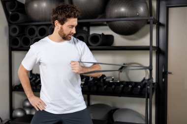 Güç egzersizi. Esmer genç sporcu elastik bantla egzersiz yapıyor ve motive olmuş görünüyor.