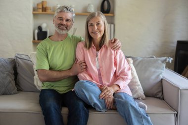 Olgun bir çift, rahat koltukları kucaklıyor. Yakınlık hissediyorlar. Evde rahat anların tadını çıkarıyorlar.