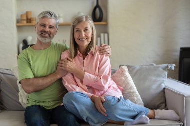 Olgun bir çift, gündelik giysiler giyip birlikte kanepede oturuyor ve birlikte hassas anların tadını çıkarıyorlar.