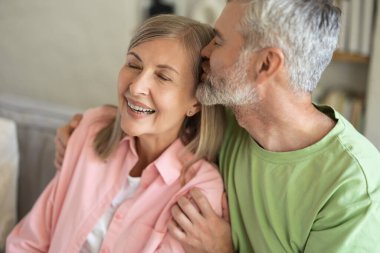 Olgun bir erkek, kadın başını öpüyor ve evde şefkat ve şefkat gösteriyor.