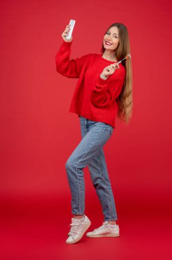 Güzellik uzmanı. Elinde yüz fırçası olan kırmızı kazaklı güzel bir kadın.