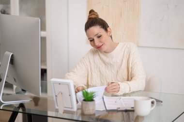 Evdeki kadın. Beyaz, sıcak kazaklı bir kadın evde, masada çalışıyor.