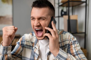 Modern ofis içinde akıllı telefonla konuşurken başarıyı kutlayan heyecanlı bir adam.