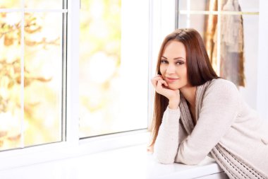 Lady is smiling genuinely while leaning on the windowsill.