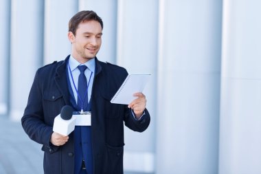 Newsman looks into his notepad while holding the microphone.