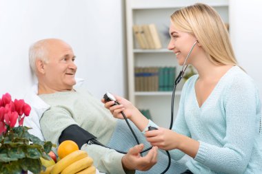Young visiting relative measures blood pressure of the patient.