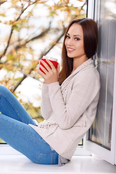 Frau auf der Fensterbank mit einer Tasse Getränk. — Stockfoto