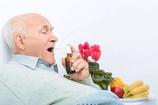 Weary senior gentleman uses his sore throat spray. — Stock Fotó