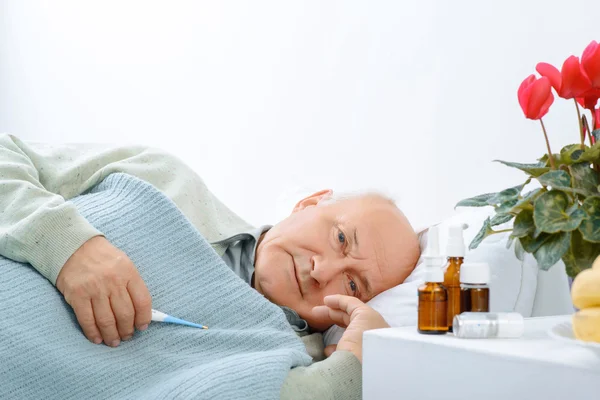 Hombre mayor de edad está descansando mientras sostiene un termómetro . — Foto de Stock