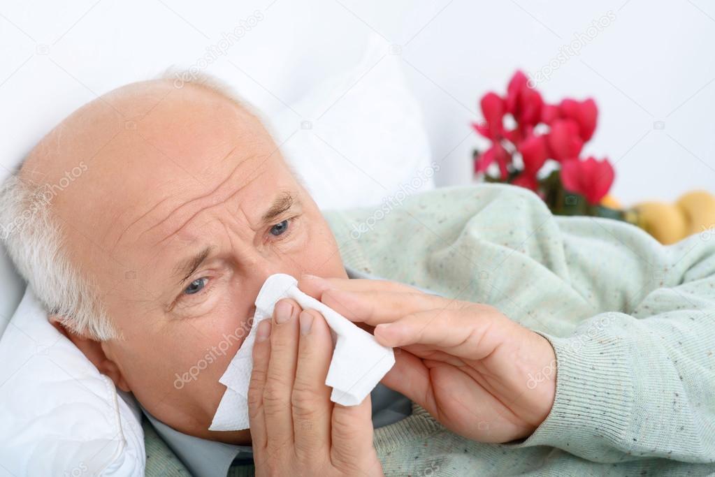 Sad exhausted old man is snorting at white handkerchief.