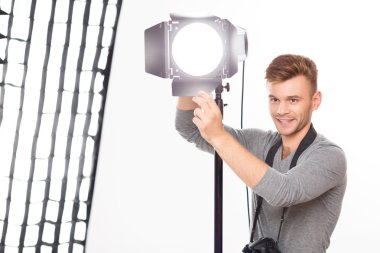 Smiling photographer is busy fixing the spotlight. clipart