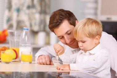 Daddy encourages his son to finish a cereal. clipart