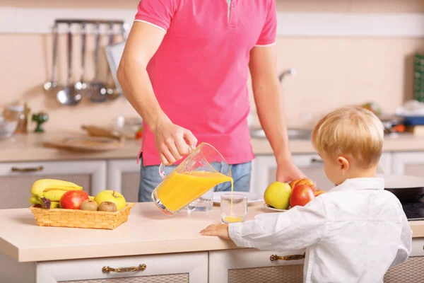 Dad pours orange juice for his son. — Stock Photo, Image