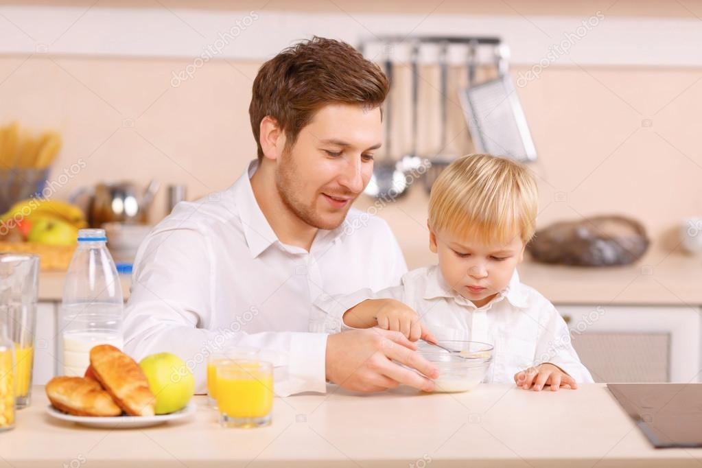 Daddy helps his son to finish a cereal.