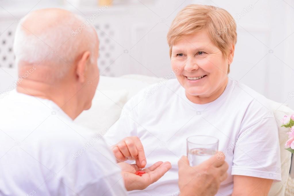 Pleasant adult husband giving pills to his wife