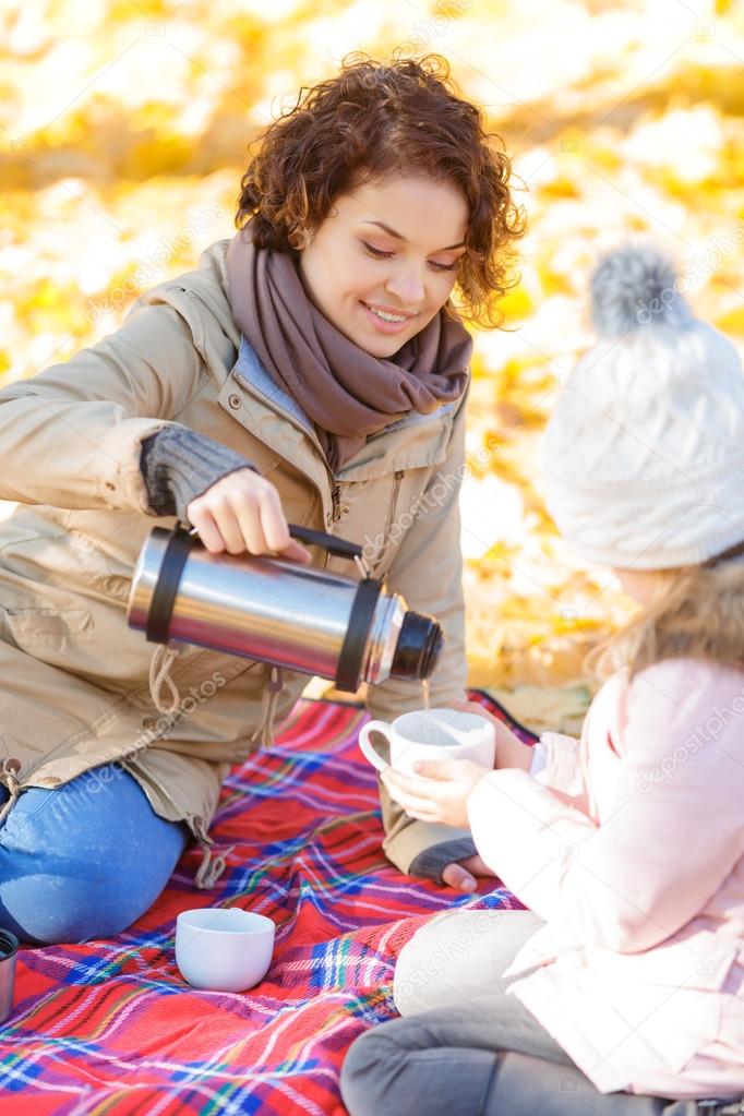 Pleasant mother and daughter drinking tea in park
