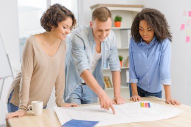 Three coworkers are working with construction drawing.