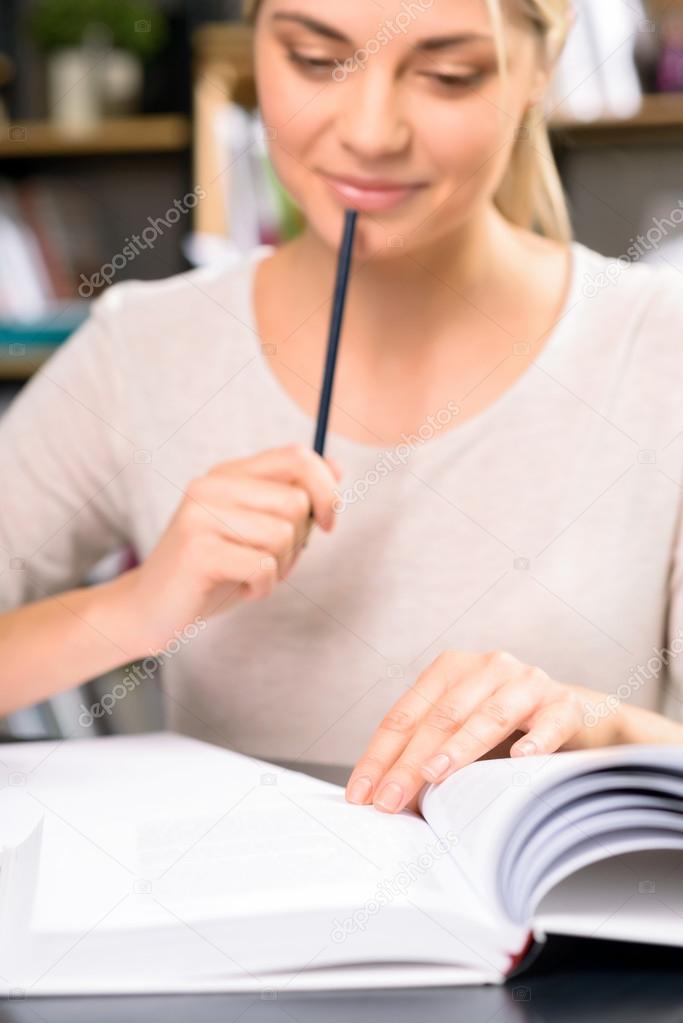 Young girl is busy reading textbook.