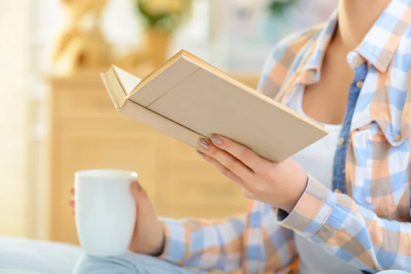 Jenta drikker te og leser bok. . – stockfoto