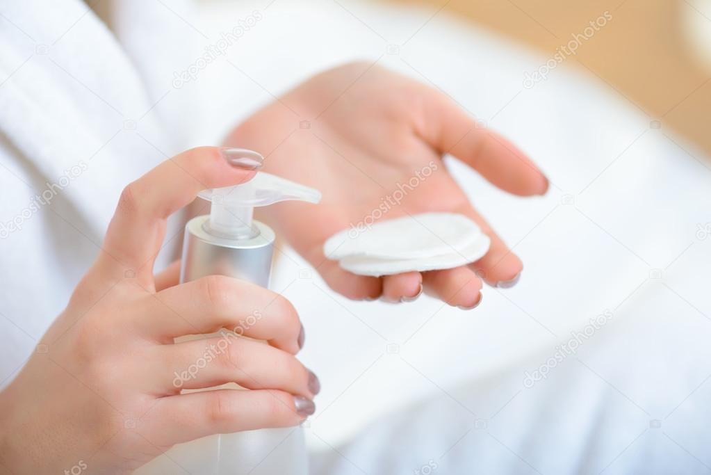Young girl putting cosmetics on cotton pad.